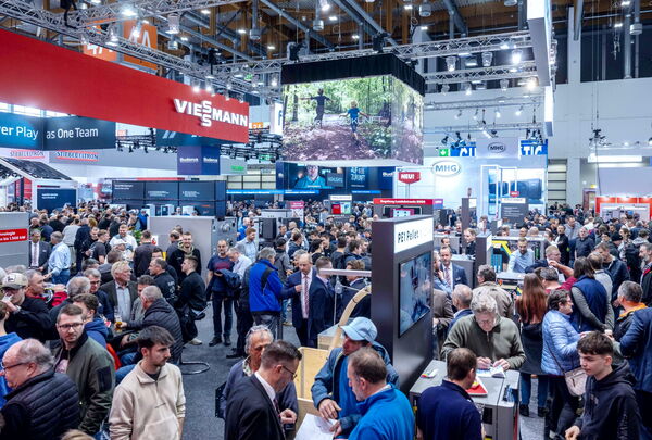 Viele Besucherinnen und Besucher bewegen sich durch eine Messehalle mit Messeständen.