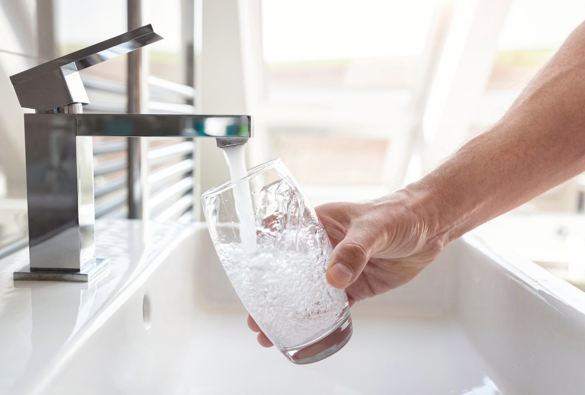 Hände füllen ein Trinkglas mit Wasser aus einem Wasserhahn